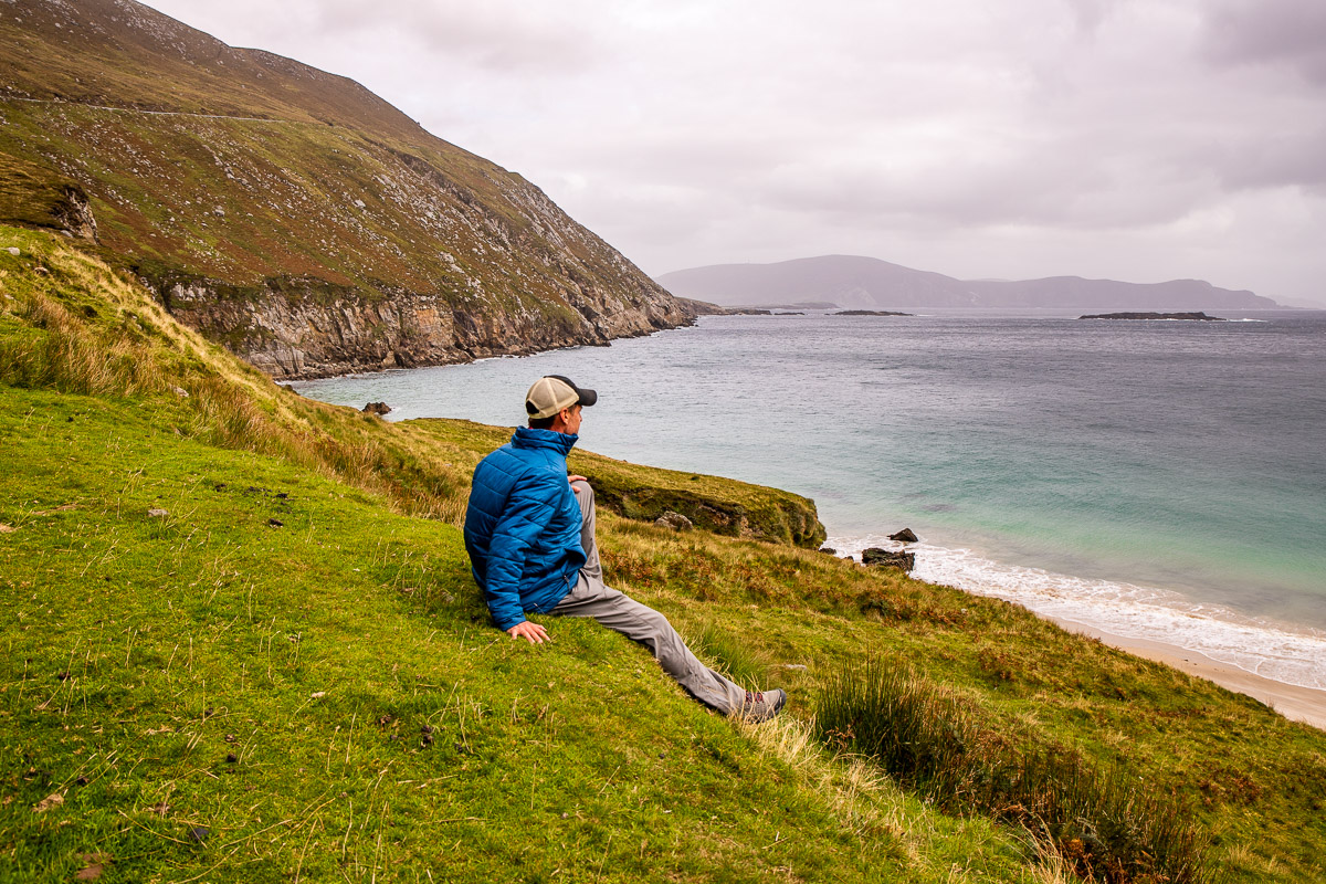 Man sitting on a cliff top overlooking a beach