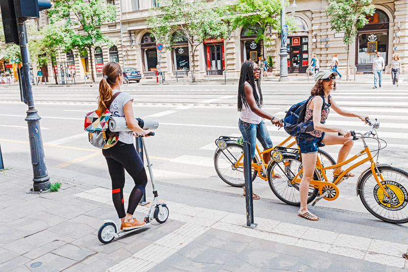 A woman on a kick scooter near the pedestrian crossing is waiting for the bicyclists to pass by, the rules of the road and traffic laws concept