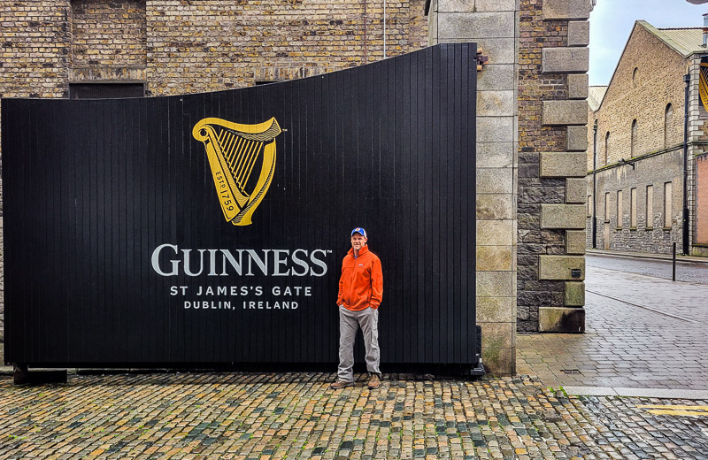 Man standing in front of a large black gate with the words Guinness