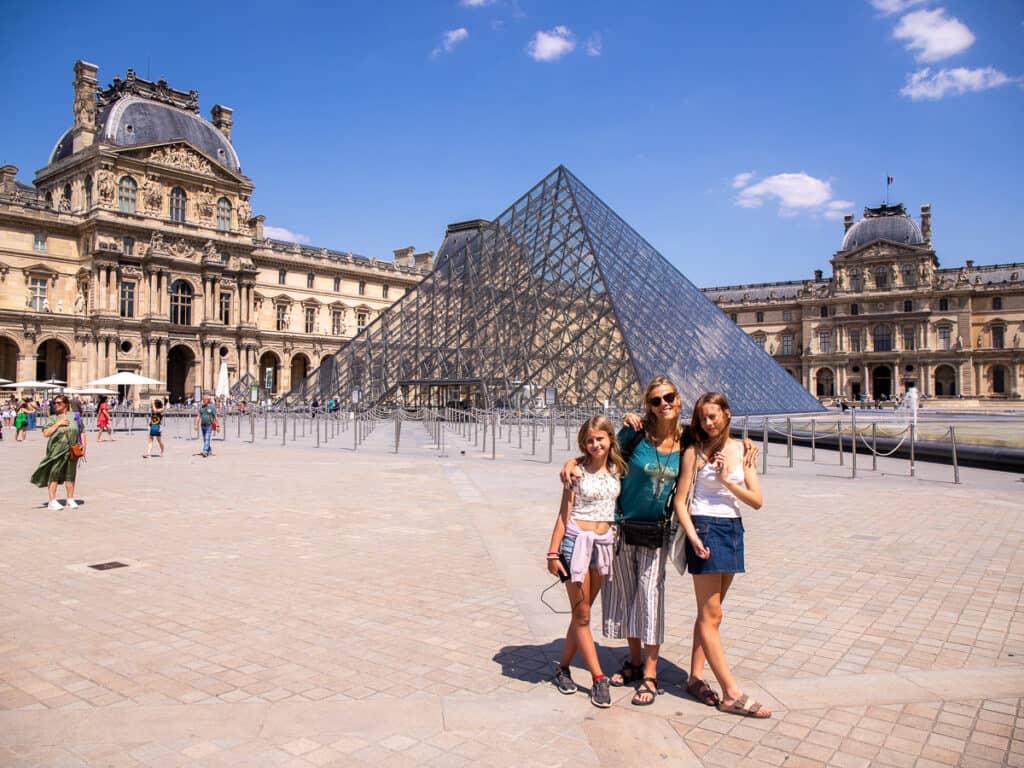 Mom and two daughters in front of a glass pyramid at the Louvre Museum in Paris