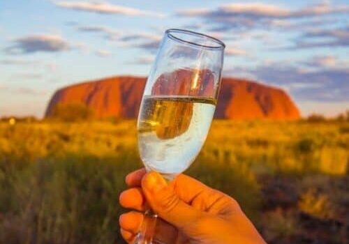 glass of champagne in front of uluru
